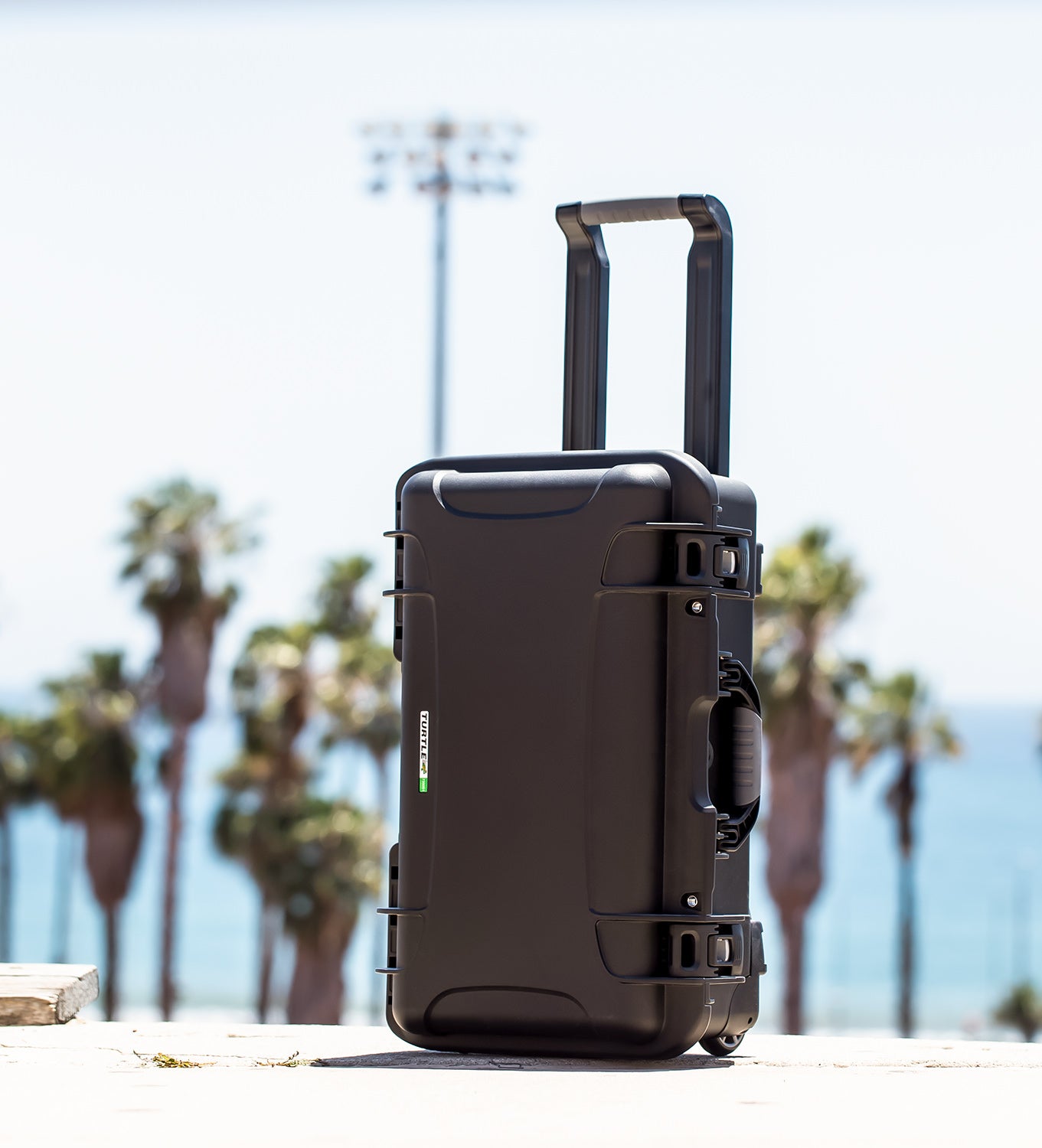 Turtle Case 735 Black Case with wheels and handle extended, palm trees and stadium lights in the background 